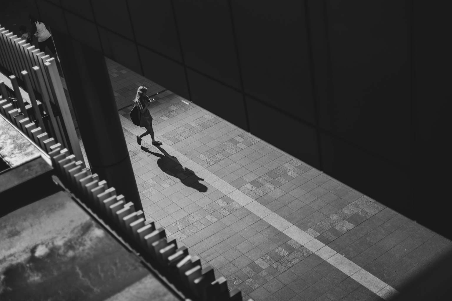 A monochrome urban scene showing a person walking with their shadow