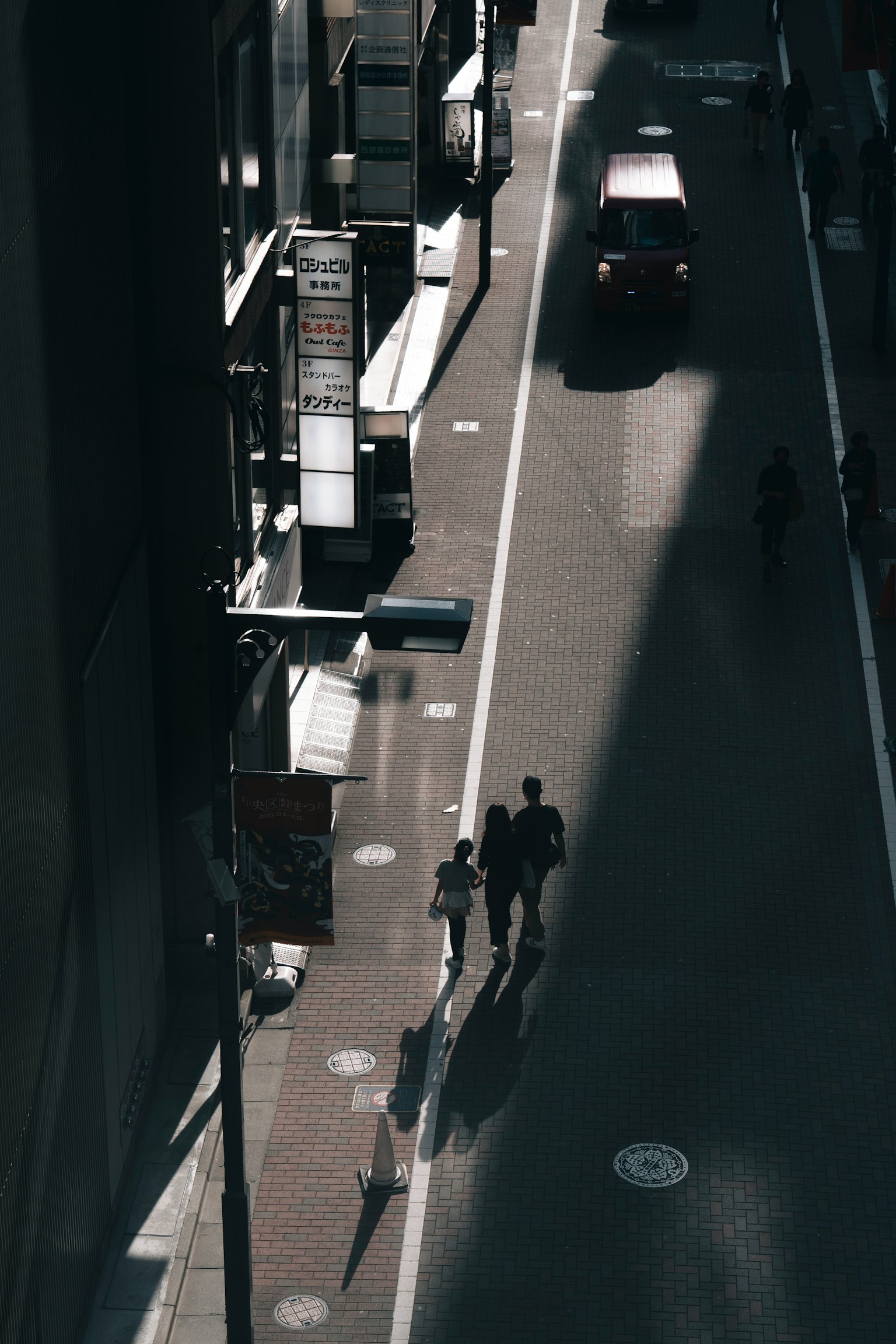 两个人在城市街道的阴影中走过，一辆车经过