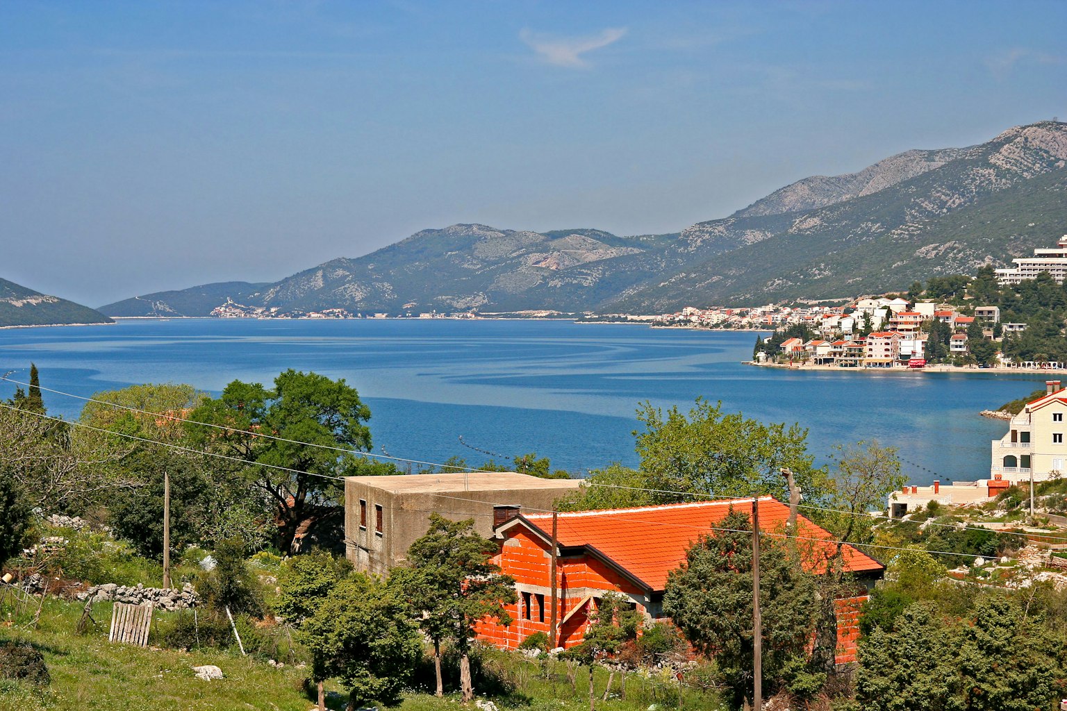 Scenic view of a house with an orange roof overlooking a blue sea and mountains