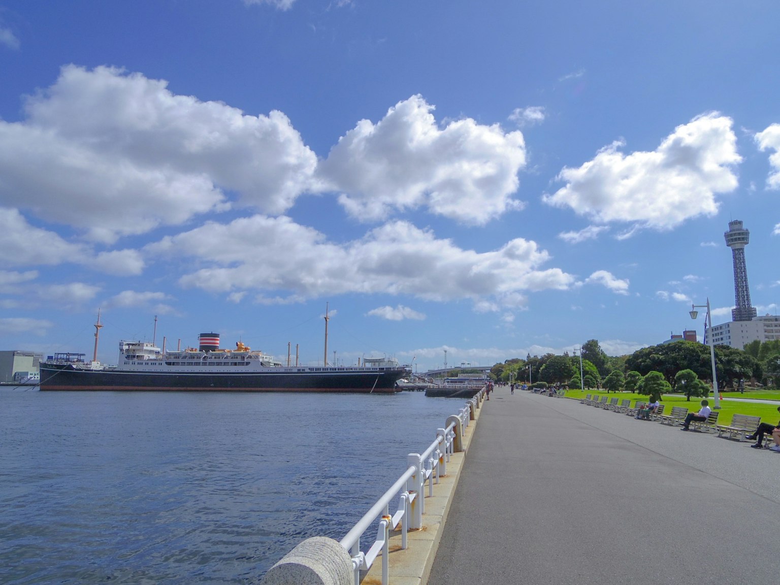 Scenic view of a waterfront promenade with a large ship and blue sky