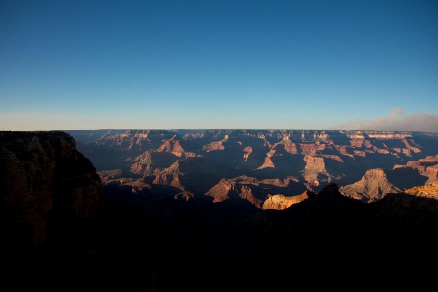 Cảnh quan rộng lớn của Grand Canyon với bầu trời xanh và bóng dáng núi