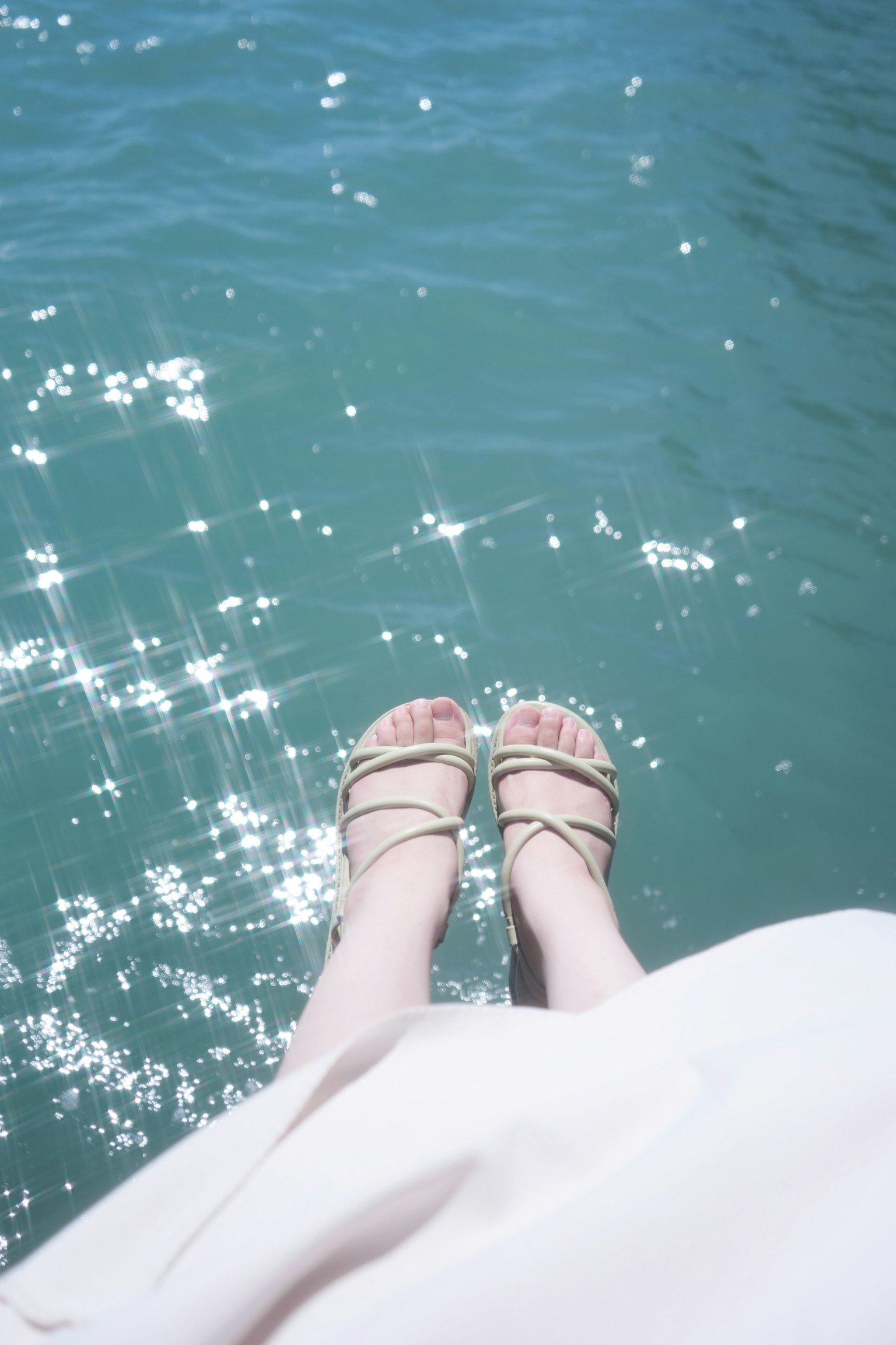 Kaki dalam sandal menggantung di atas air biru berkilau