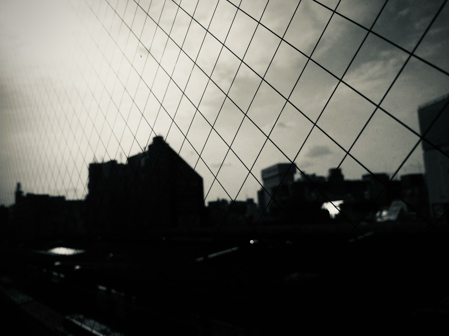 黒いシルエットの都市景観と網目状のガラスの反射