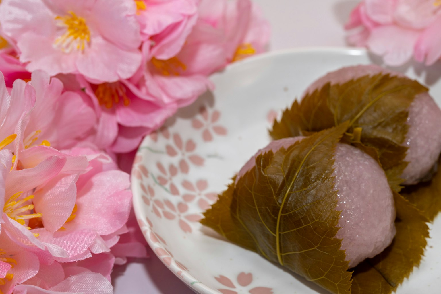 Plato de dulces japoneses envueltos en hojas junto a flores de cerezo rosas