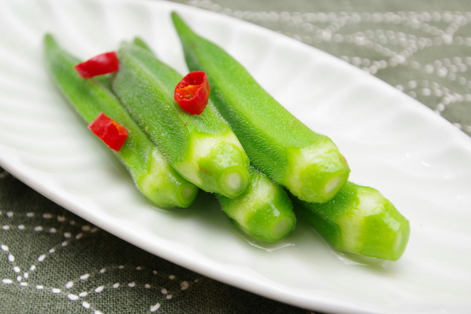 Frische grüne Okra und rote Chilischoten auf einem weißen Teller
