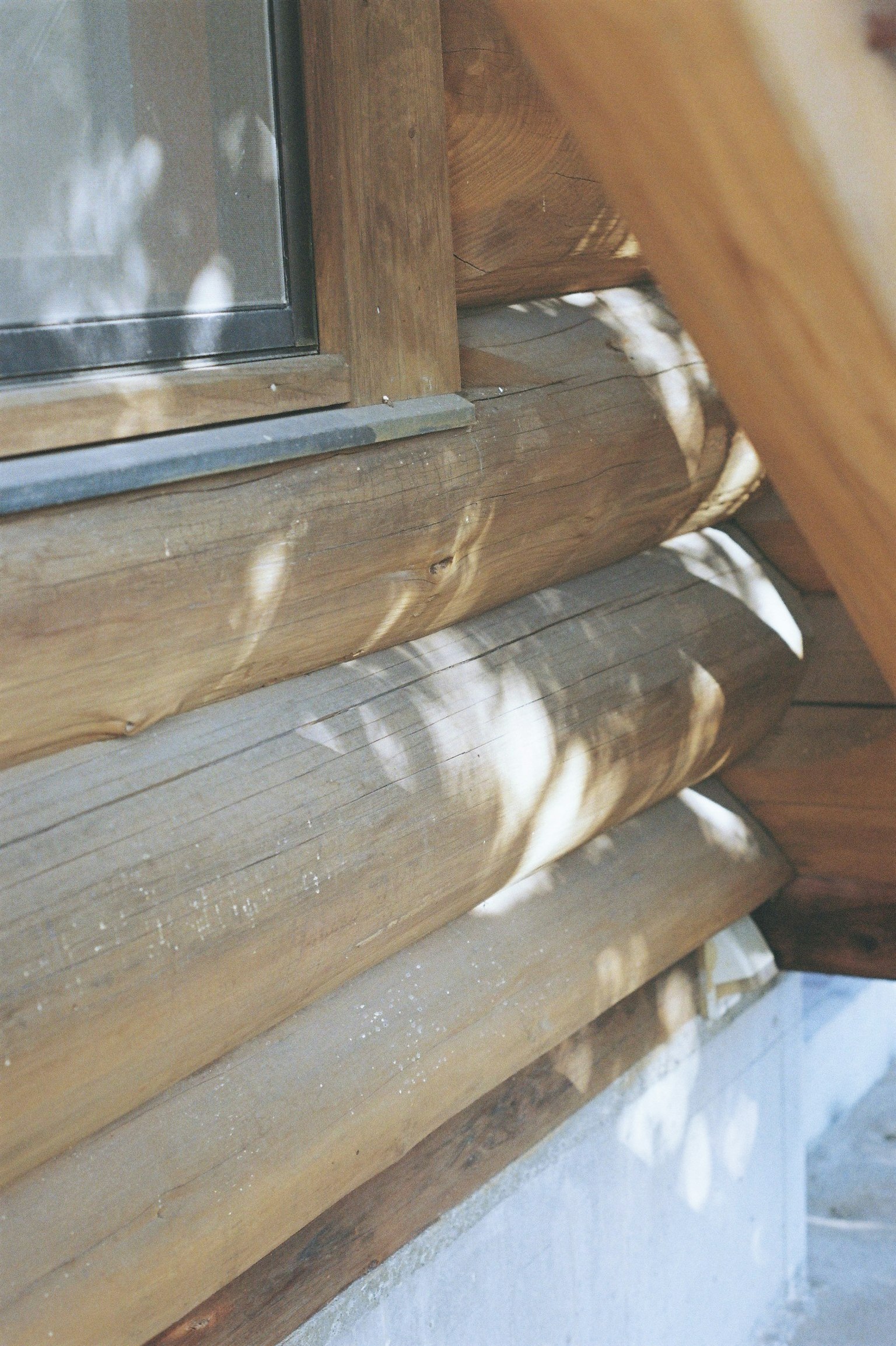 Close-up view of wooden log cabin wall with window and soft shadows