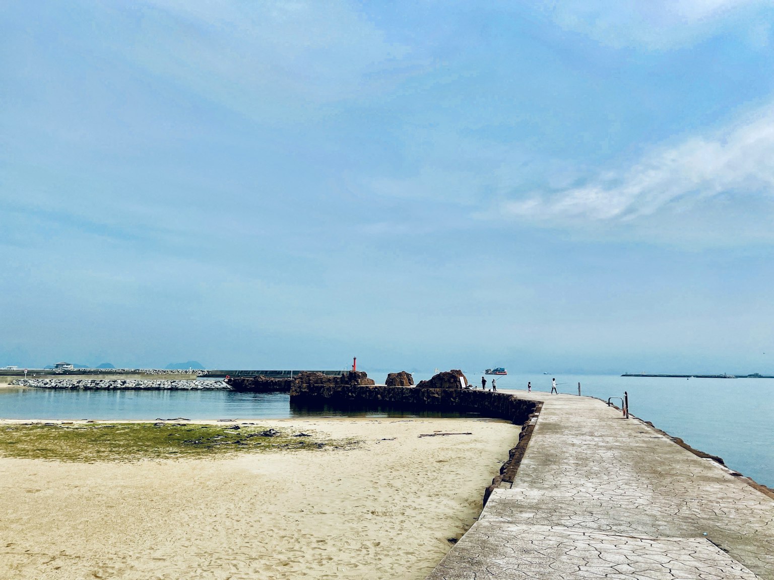 Scena di spiaggia tranquilla con mare calmo e cielo blu Molo in cemento che si estende nell'acqua