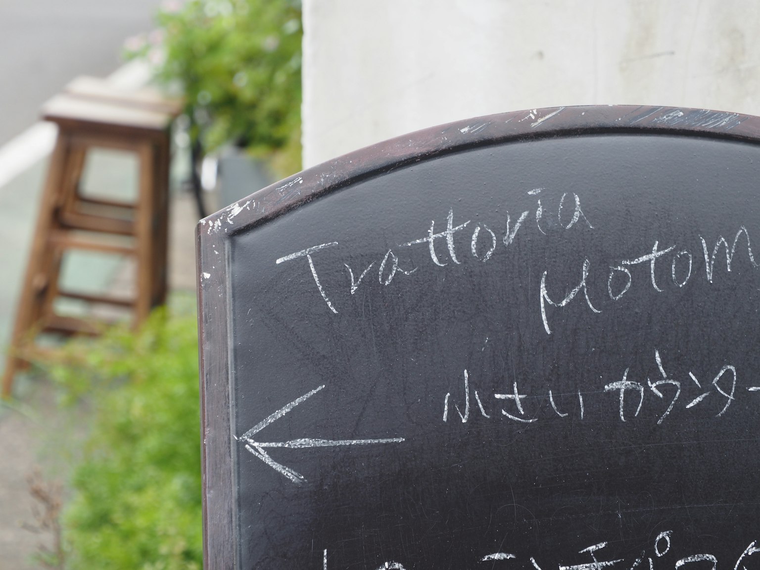 Un panneau en ardoise pour Trattoria Motom avec une flèche pointant à gauche