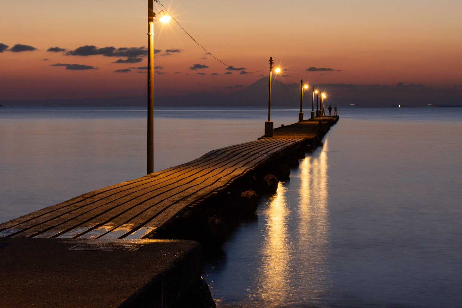 夕暮れ時の桟橋に灯る街灯と静かな水面