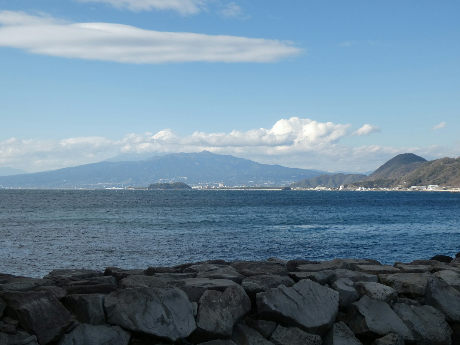Pemandangan laut biru dan pegunungan dengan breakwater batu