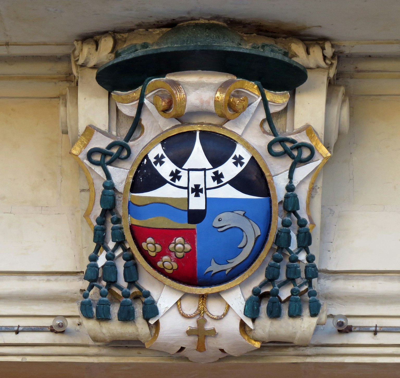 Coat of arms featuring a dolphin and floral designs on a blue shield adorned with golden decorations and green ribbons