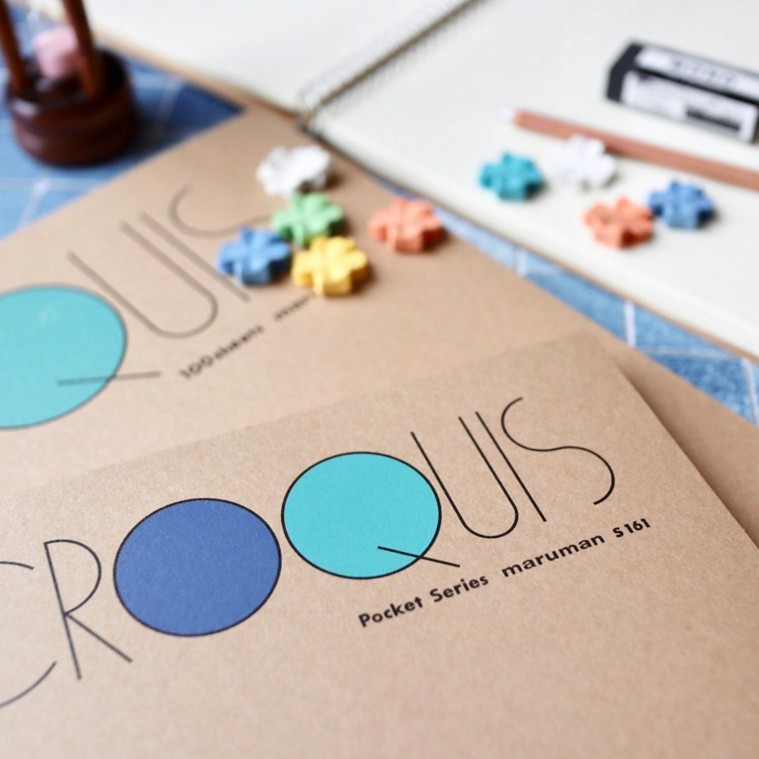 Cuaderno de bocetos con círculo azul y cubierta marrón que presenta piezas de rompecabezas coloridas