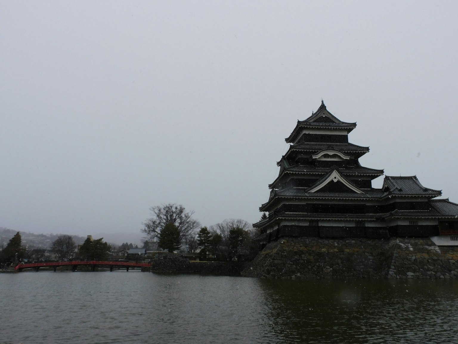 松本城在湖邊的冬季風景，黑色建築和周圍的雪