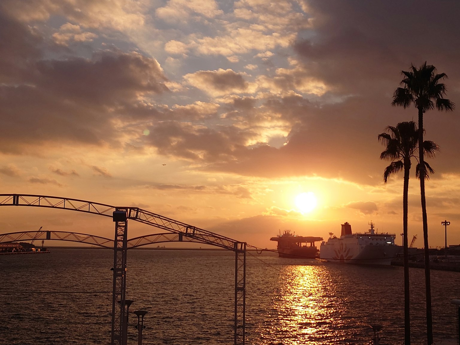 ทิวทัศน์พระอาทิตย์ตกที่สวยงามเหนือมหาสมุทร มีต้นปาล์มและเรือ
