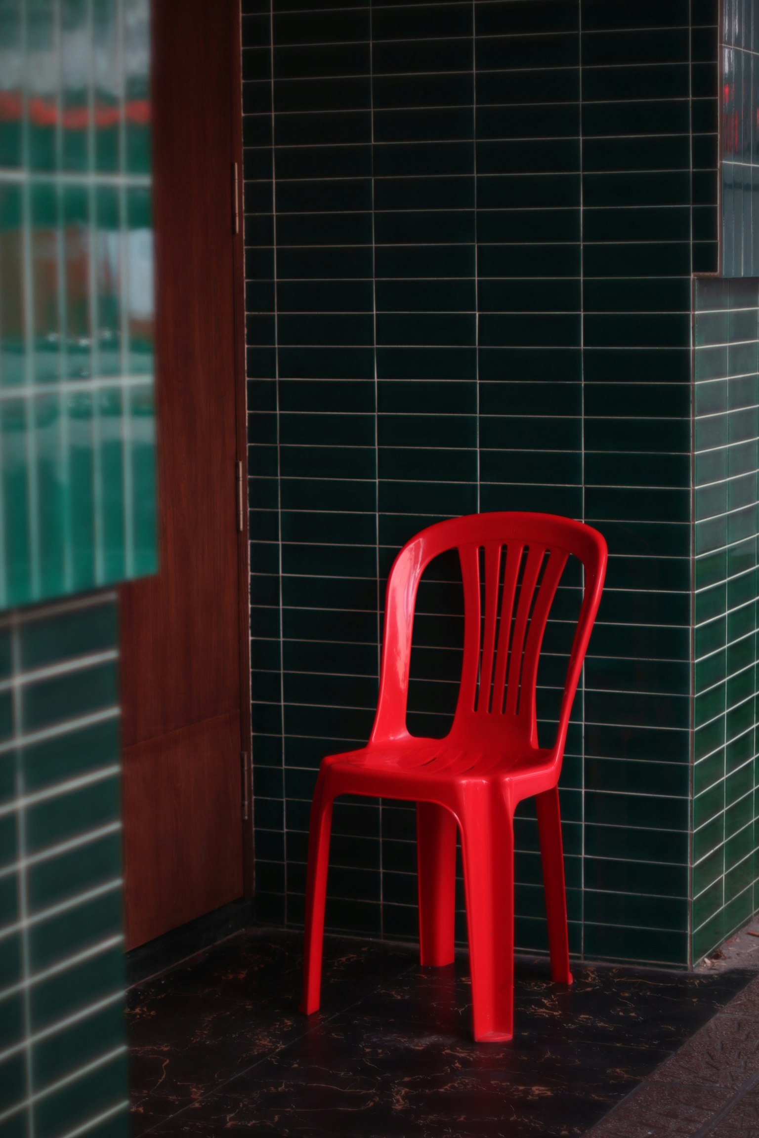緑のタイルの壁の前に置かれた赤いプラスチックの椅子