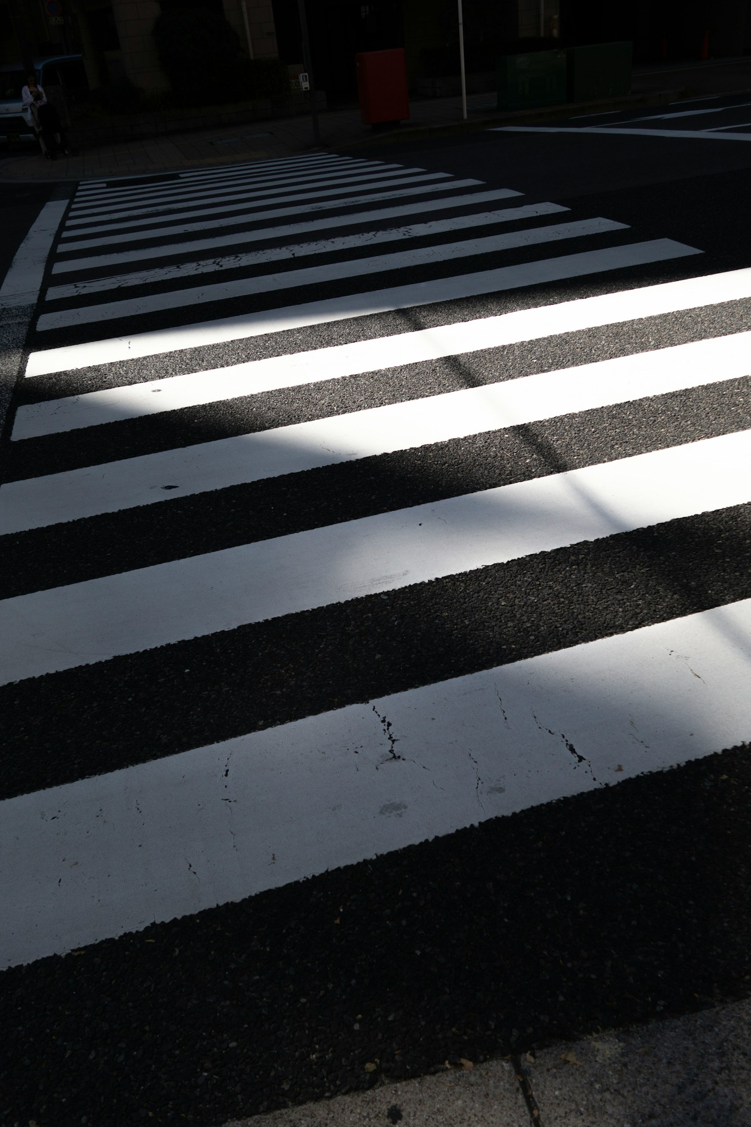 Una foto di un attraversamento pedonale a strisce bianche e nere con contrasto di luce e ombra
