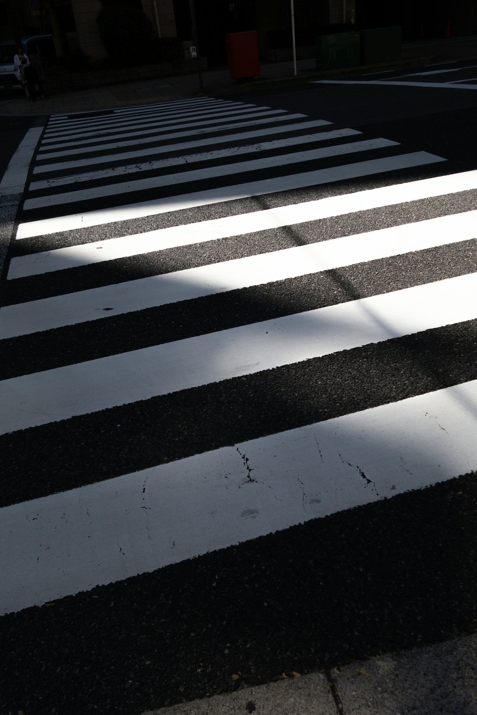 Una foto di un attraversamento pedonale a strisce bianche e nere con contrasto di luce e ombra