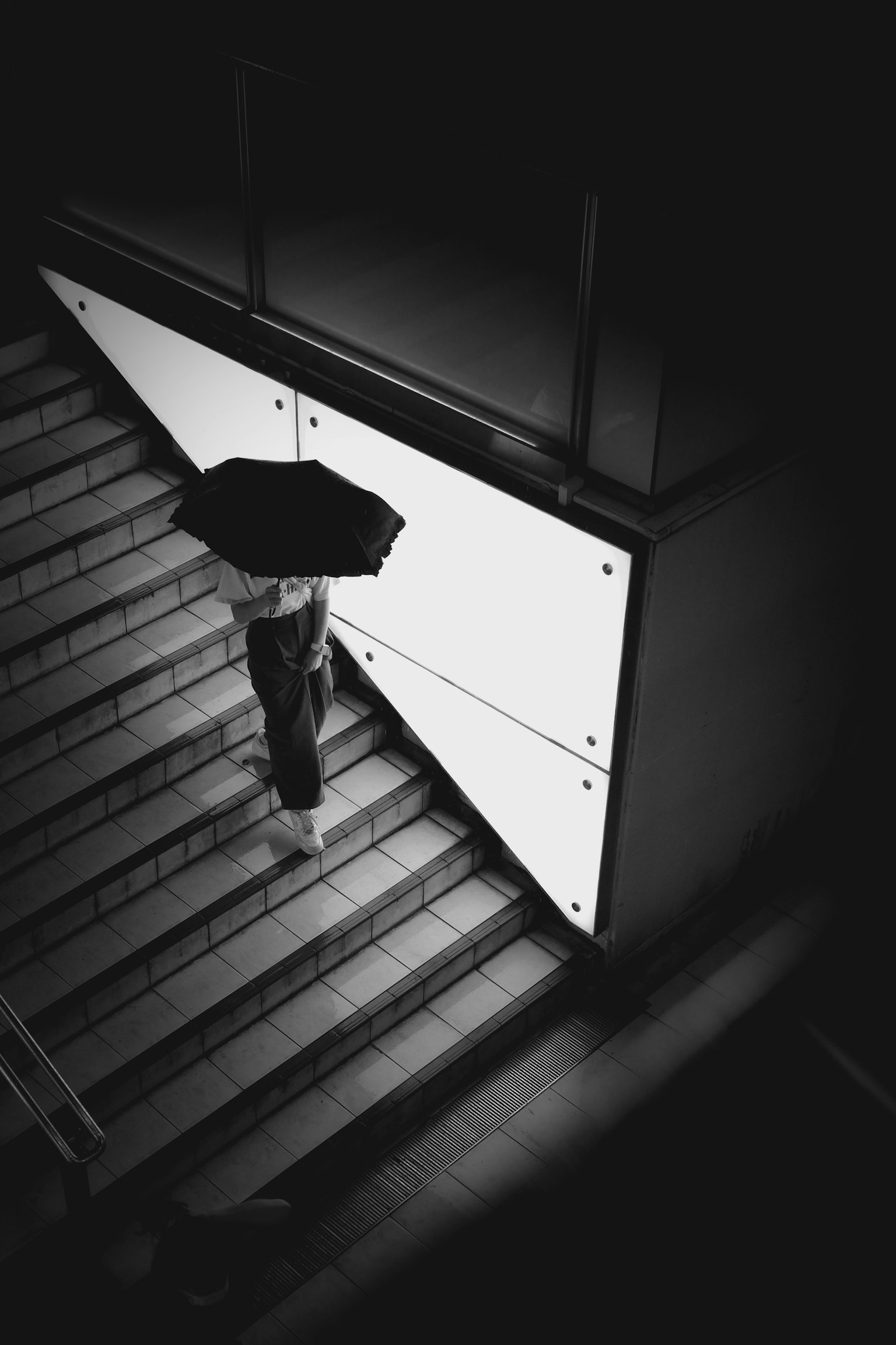 Photo en noir et blanc d'une personne descendant des escaliers avec un parapluie Fond lumineux avec des ombres sombres