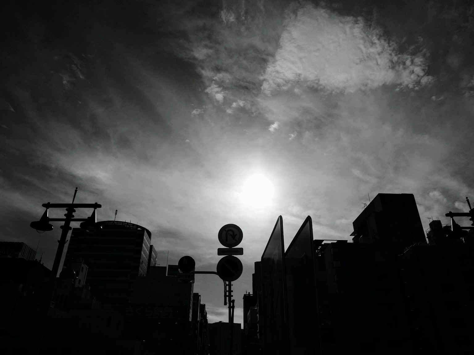 Cielo en blanco y negro con un sol brillante y edificios en silueta
