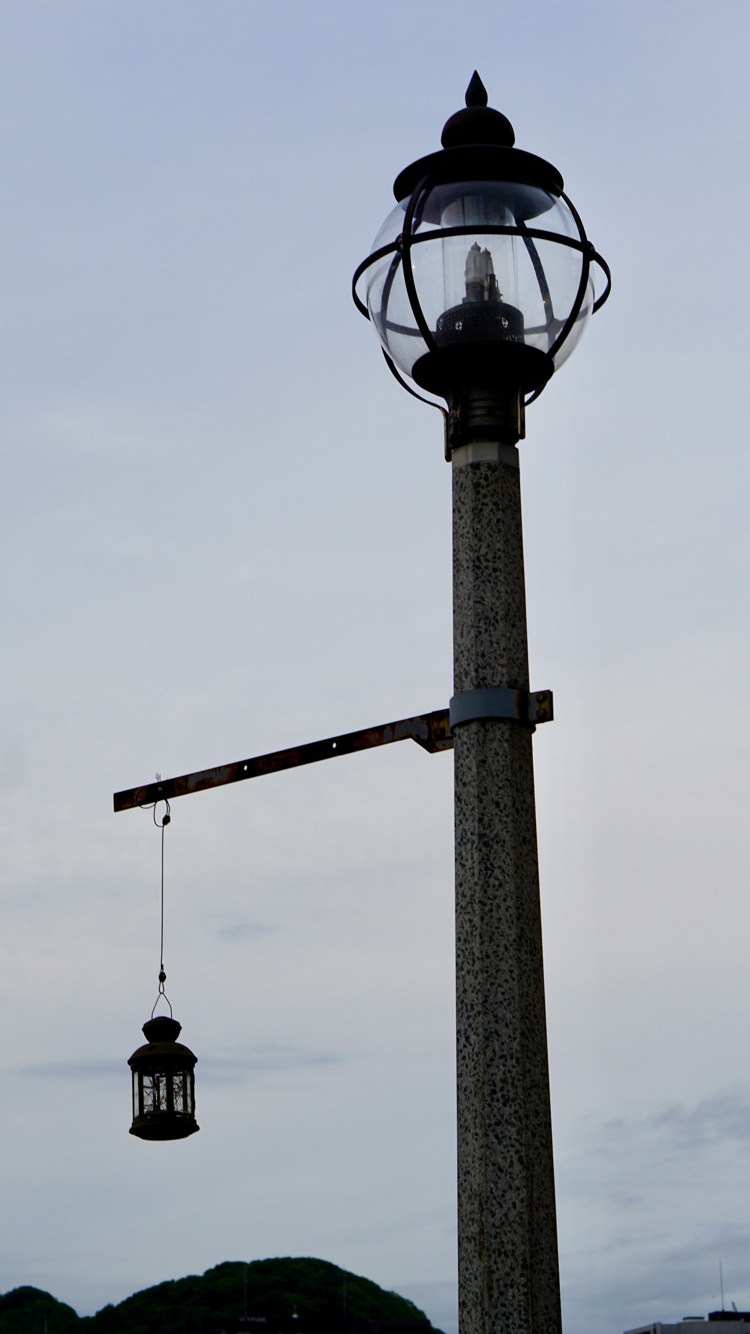 Laternenmast mit hängender Laterne vor einem grauen Himmel