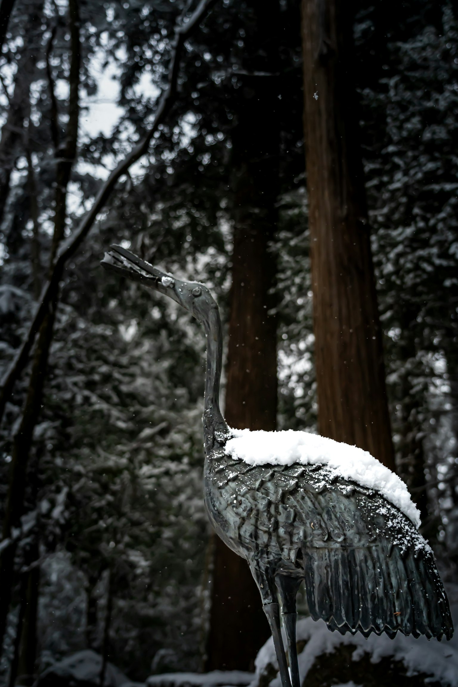一座被雪覆盖的鹤雕像矗立在雪-covered森林中