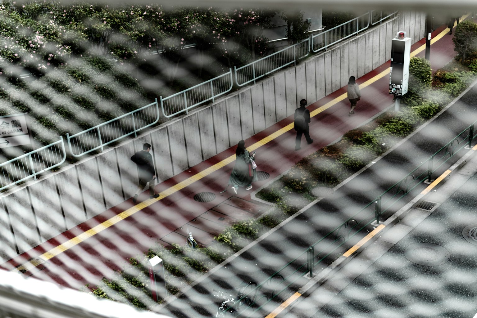 People walking along a pathway with greenery viewed through a mesh fence