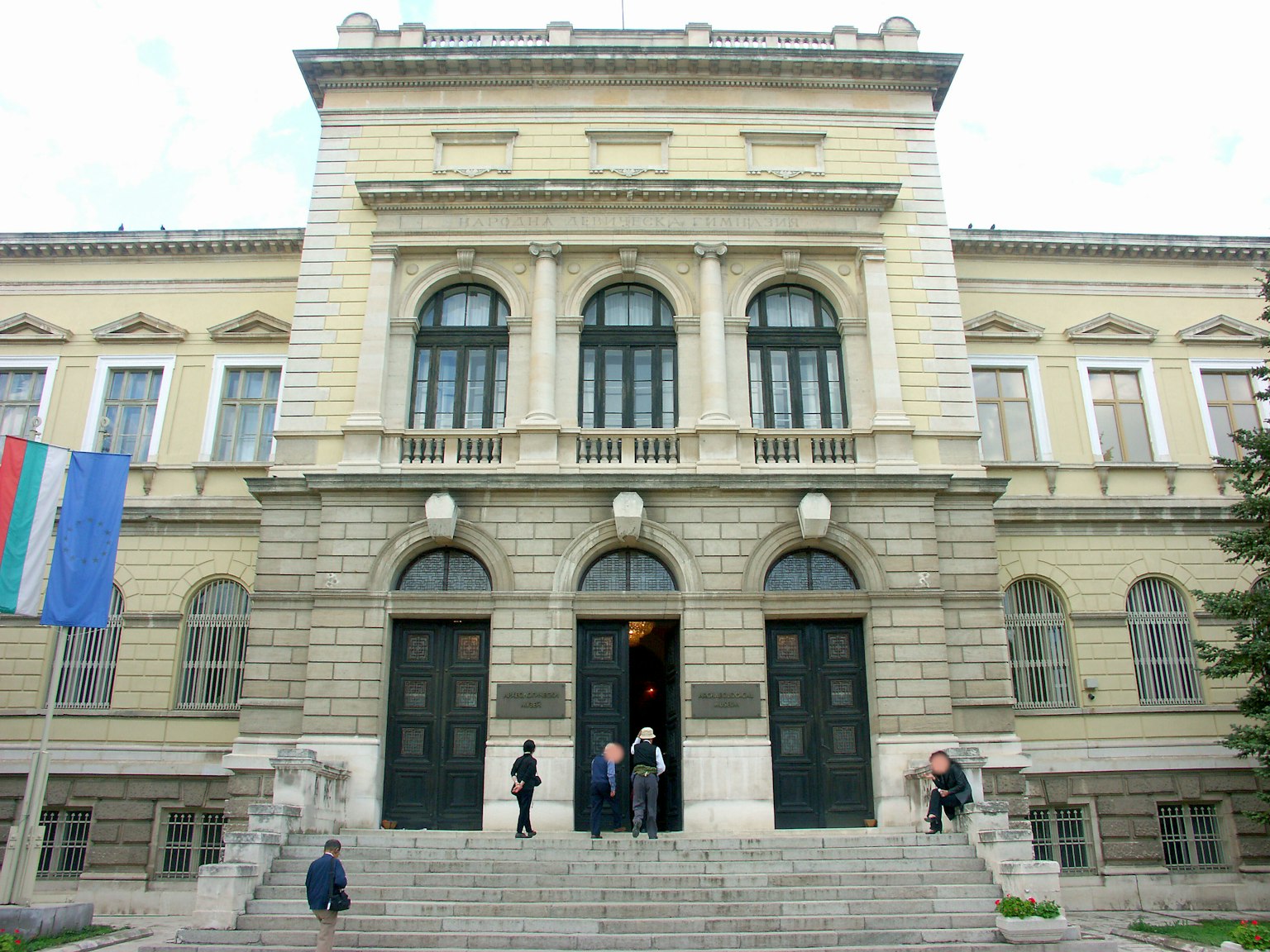 Historic building facade with people at the entrance and flags