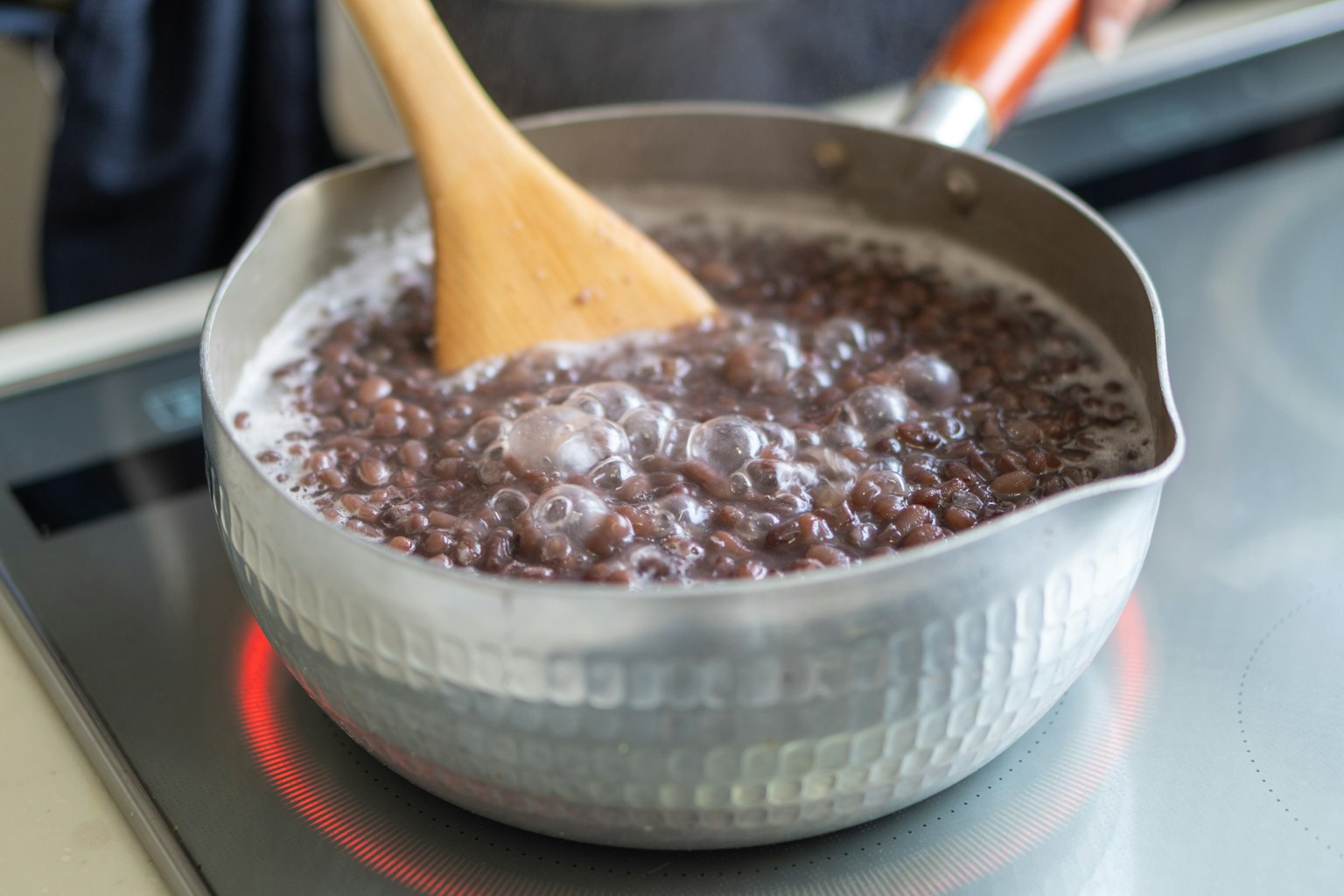 Imagen de frijoles negros hirviendo en una olla siendo removidos con una cuchara de madera