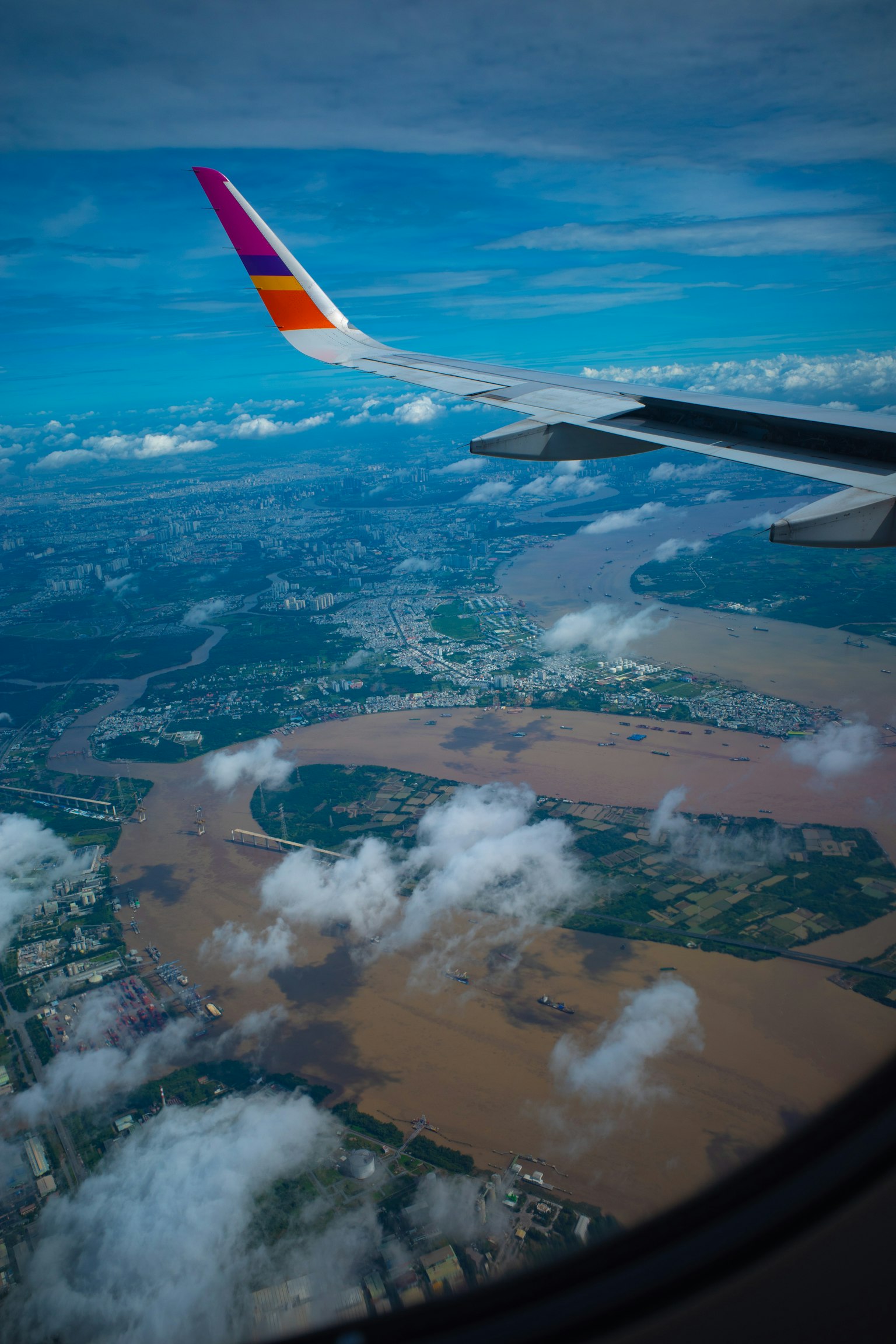 Airplane wing above swirling river and green landscape under blue sky