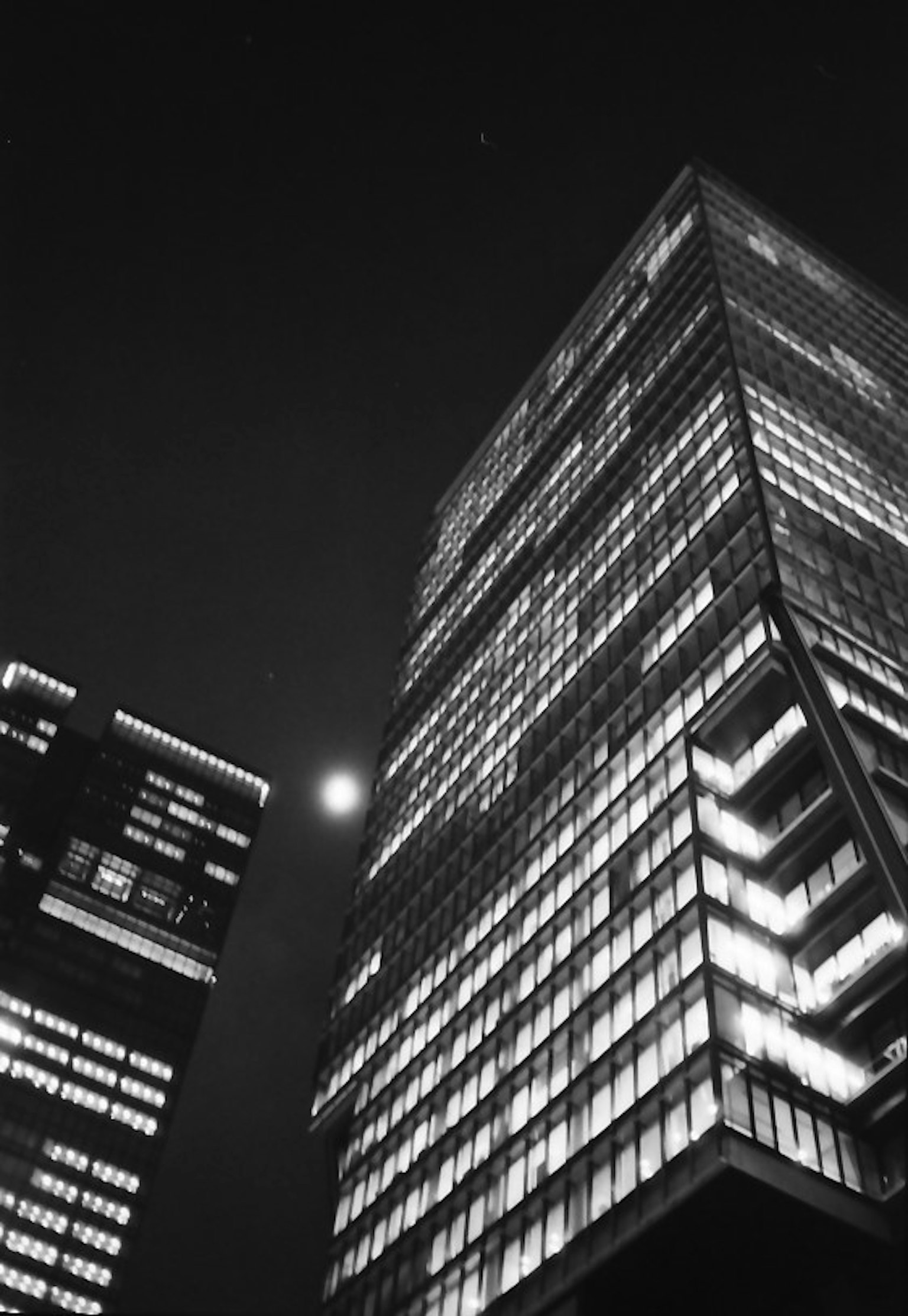 Immagine notturna di grattacieli con finestre illuminate e una luna visibile
