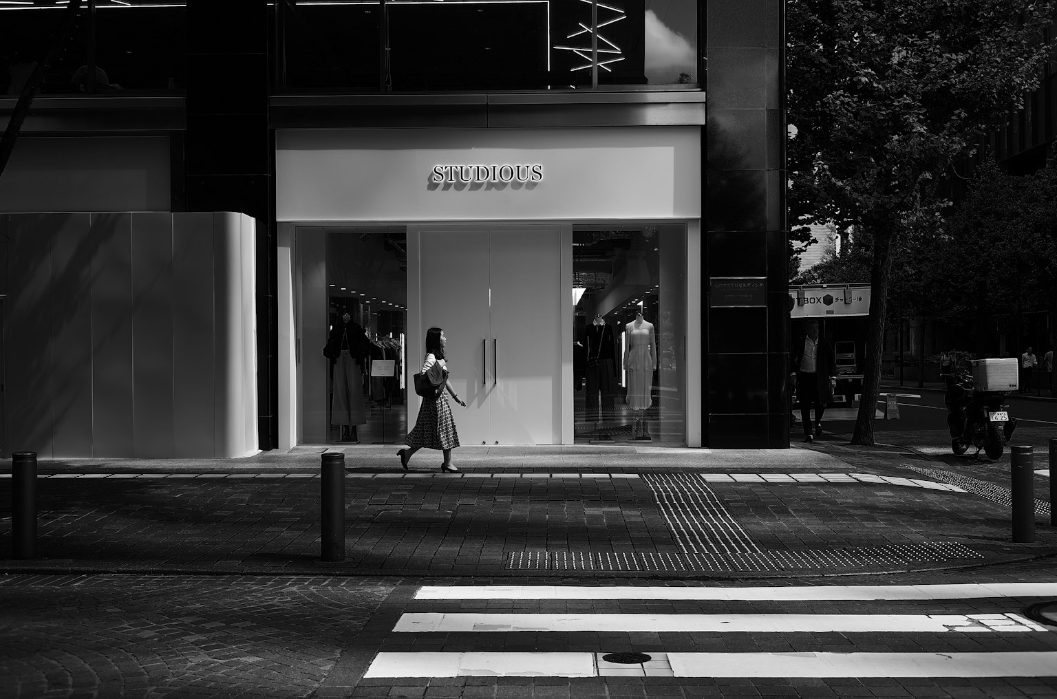 Una mujer caminando en una escena de calle en blanco y negro frente a una tienda