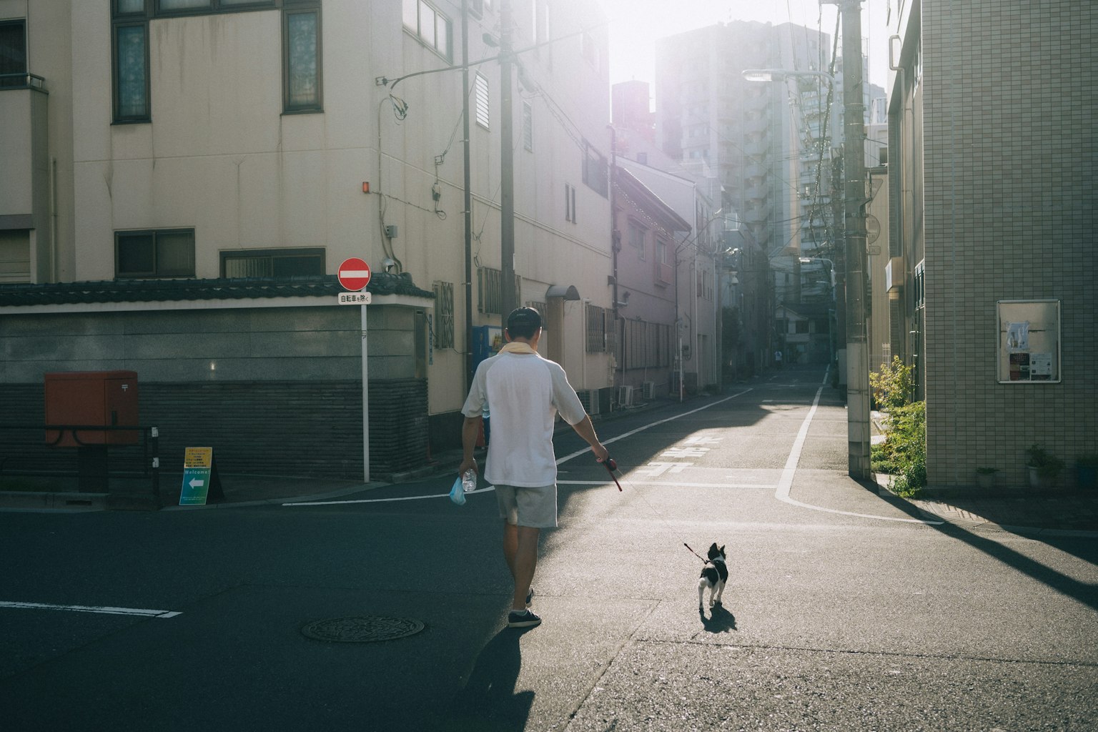 Un hombre paseando a un perro en una calle estrecha con luz