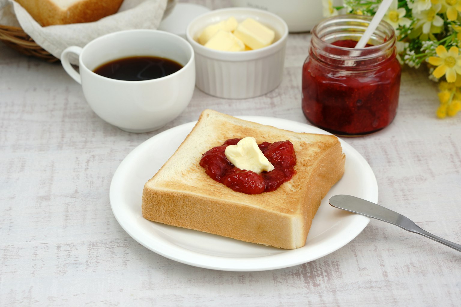 Breakfast scene featuring toast with butter and jam coffee and butter cream in the background