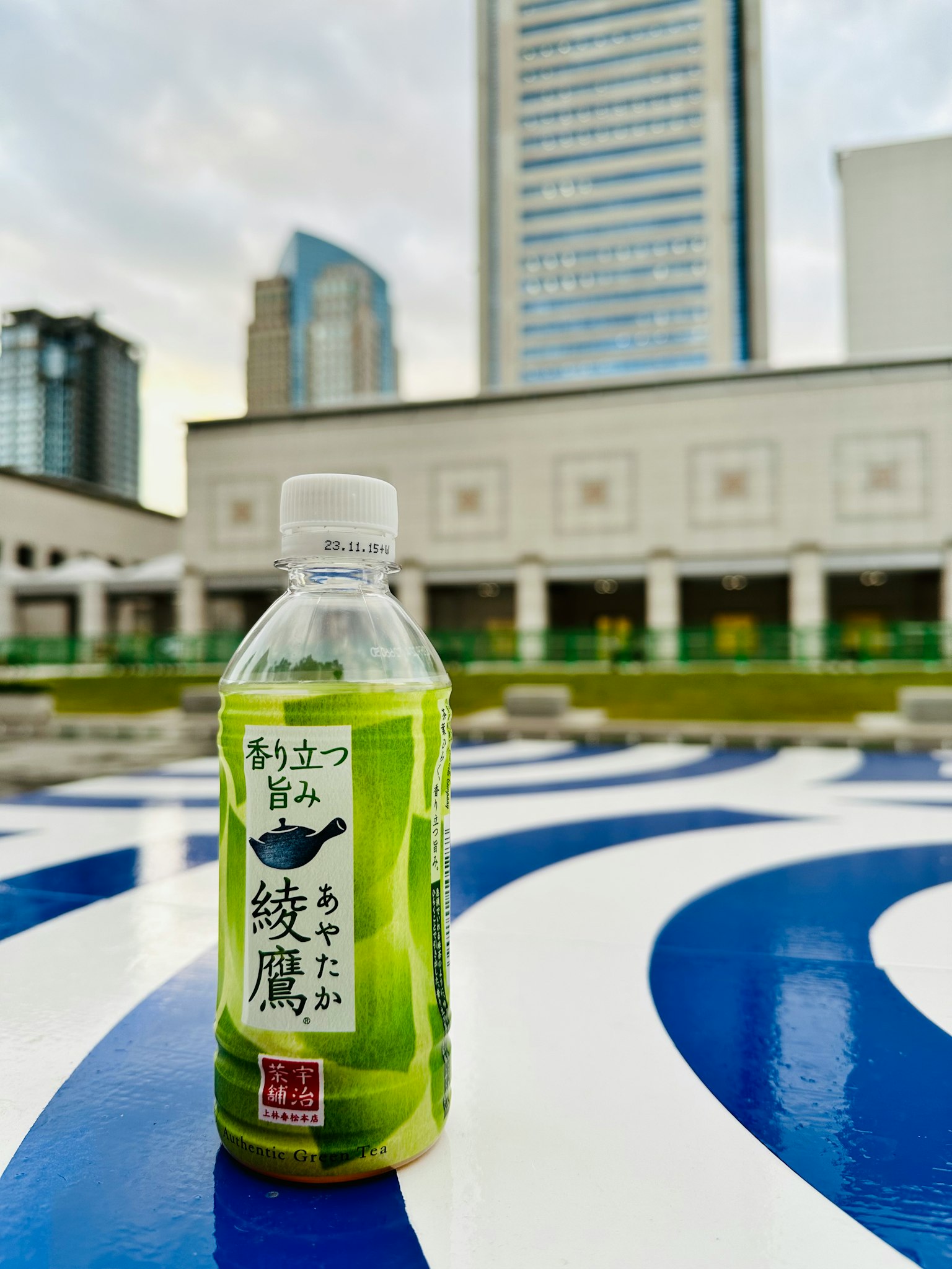 一瓶绿茶放在蓝白色图案的表面上，背景是摩天大楼