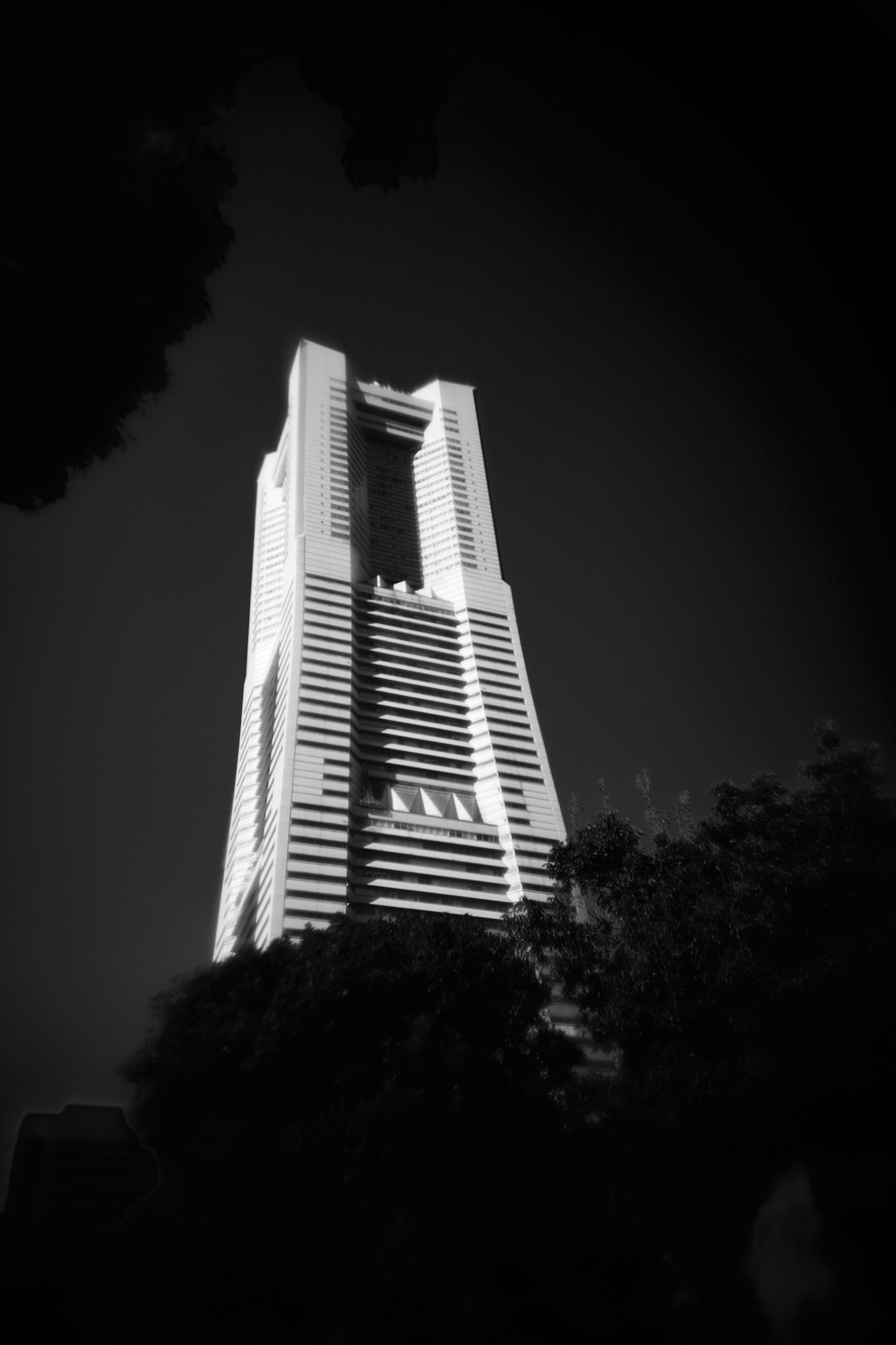 Schwarzweißfoto eines Wolkenkratzers mit einzigartigem architektonischen Design und umliegenden Bäumen