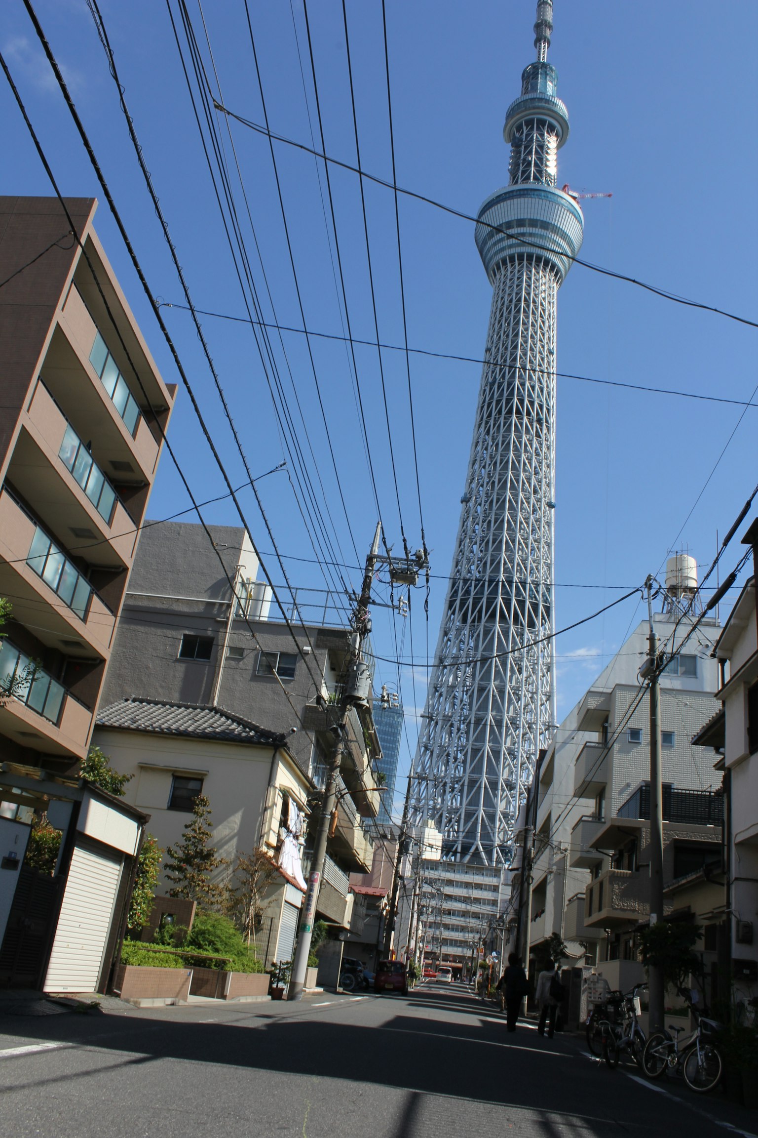 Foto Tokyo Skytree terlihat dalam pemandangan jalan di bawah langit biru dengan kabel listrik