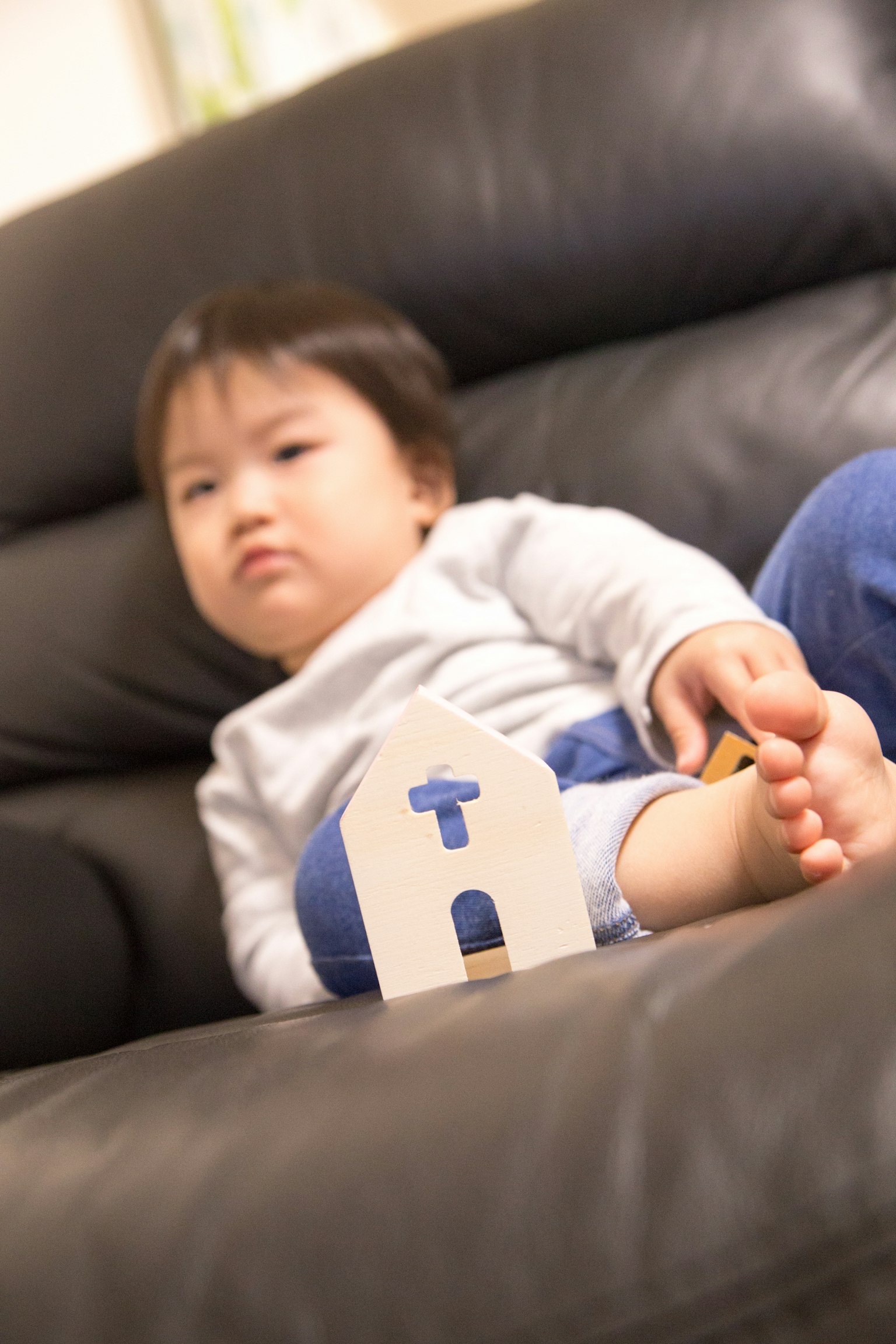 Child sitting on a sofa with a wooden house toy