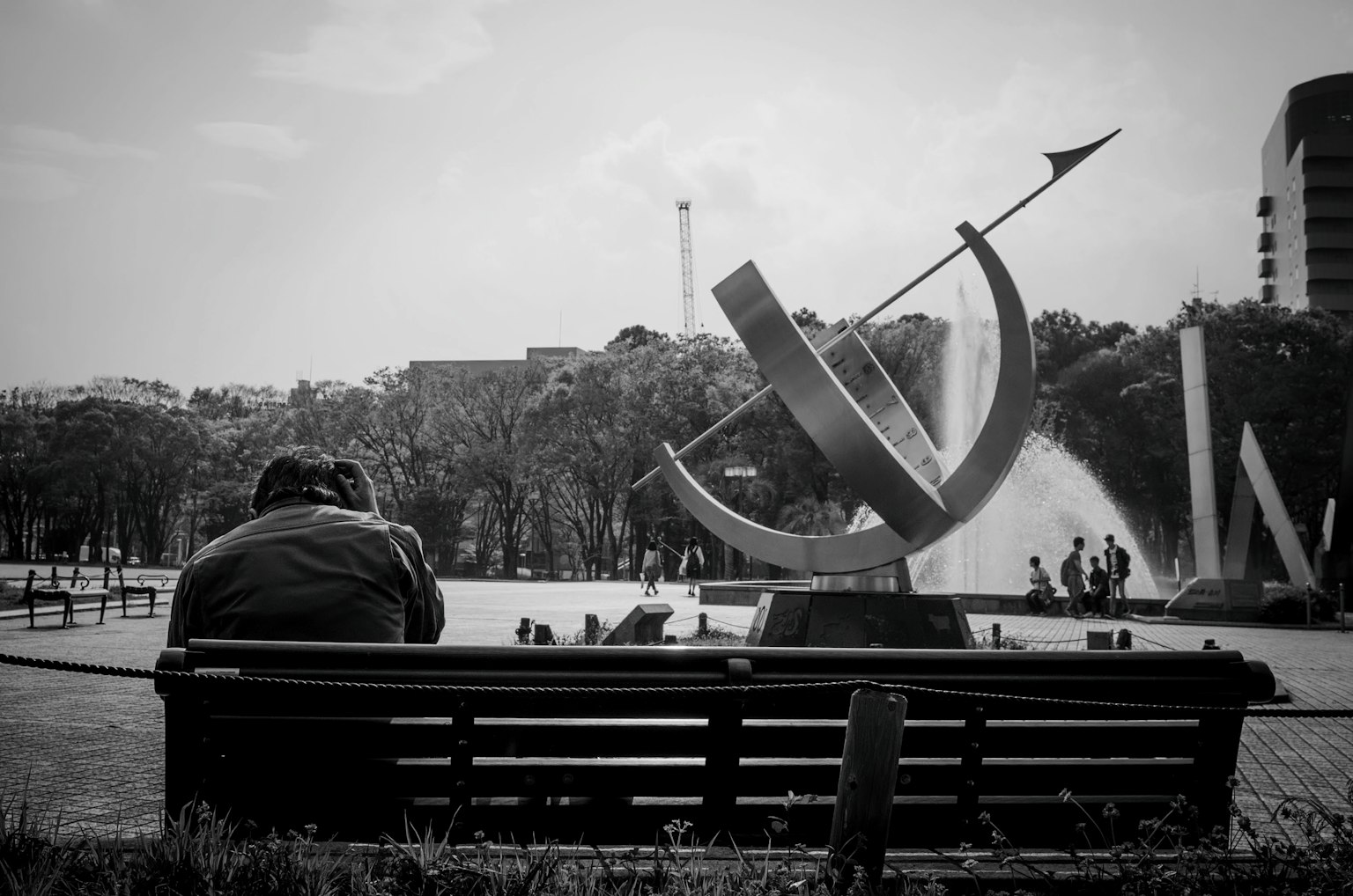 Persona sentada en un banco del parque con una escultura y una fuente
